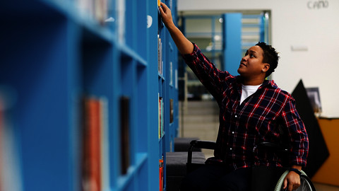 Man in een rolstoel voor een boekenkast waar hij een boek uit pakt